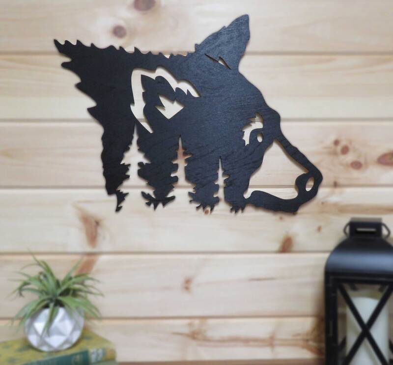 Wood black bear head with tree silhouette cutouts painted black and hung on pine wall.