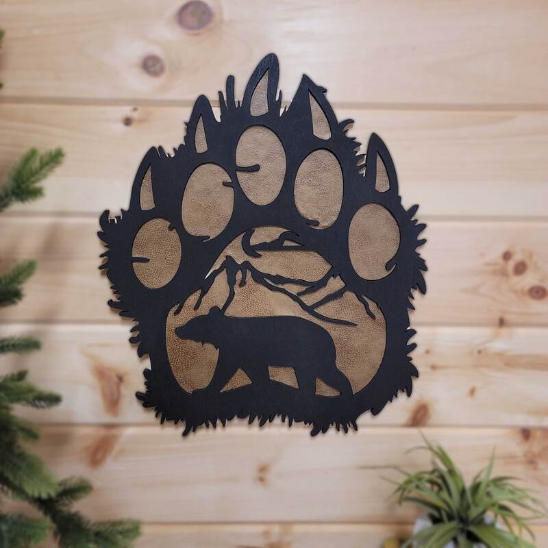 Bear paw print with mountain and bear silhouette painted black with faux suede insert on pine wall.