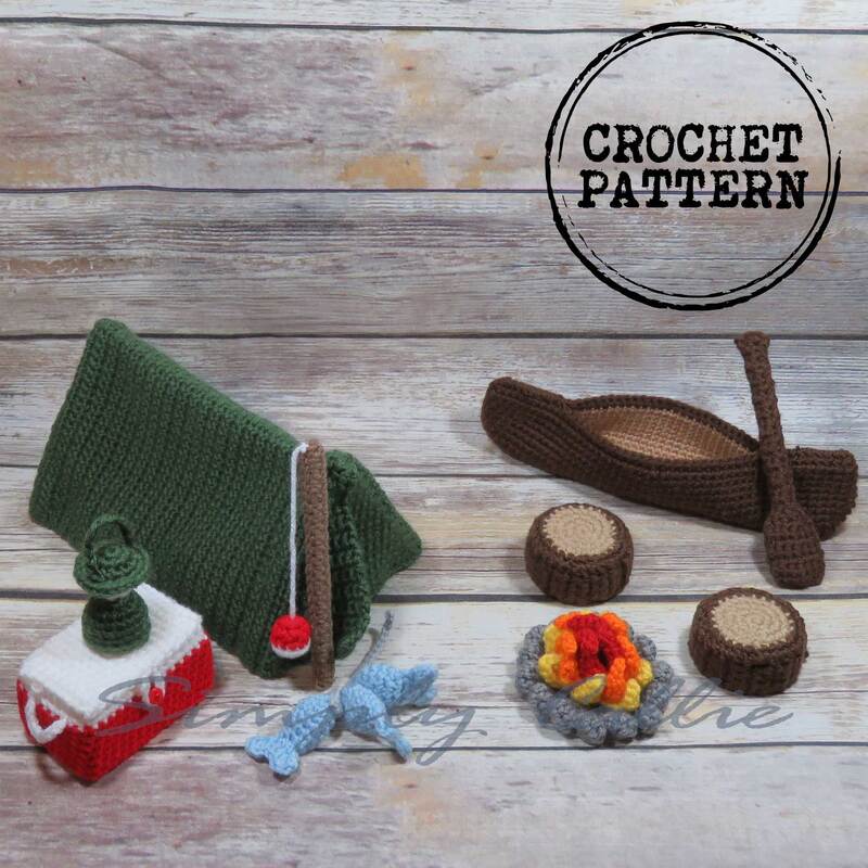 Crochet camping pattern playset that includes a tent, canoe with paddle, fishing pole with fish, cooler, lantern, campfire and log seats.