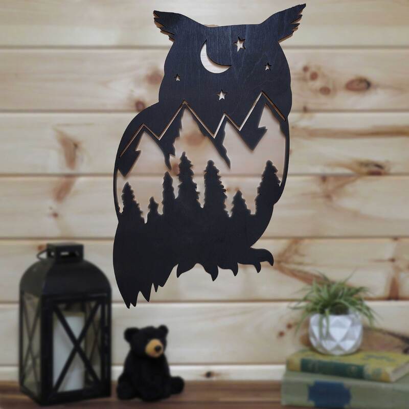 Owl silhouette with night sky, mountains and tree scene painted black on pine wall.