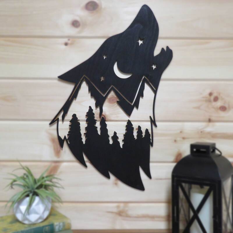 Wolf head silhouette with night sky, mountains and tree scene painted black on pine wall.